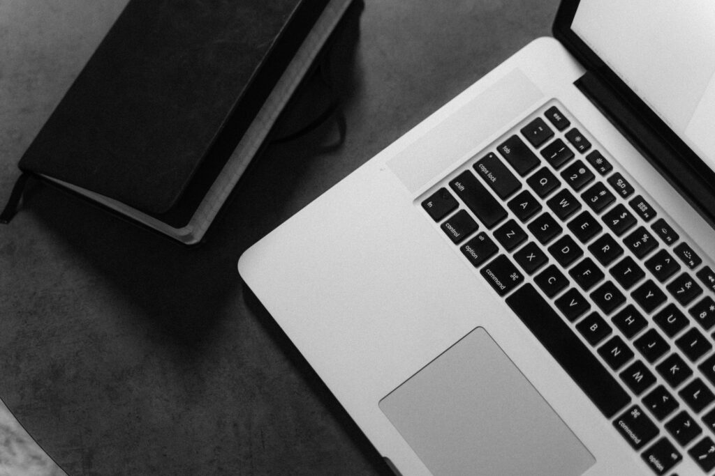 Black and white photo of a laptop and notebook on a desk, ideal for workspace themes.